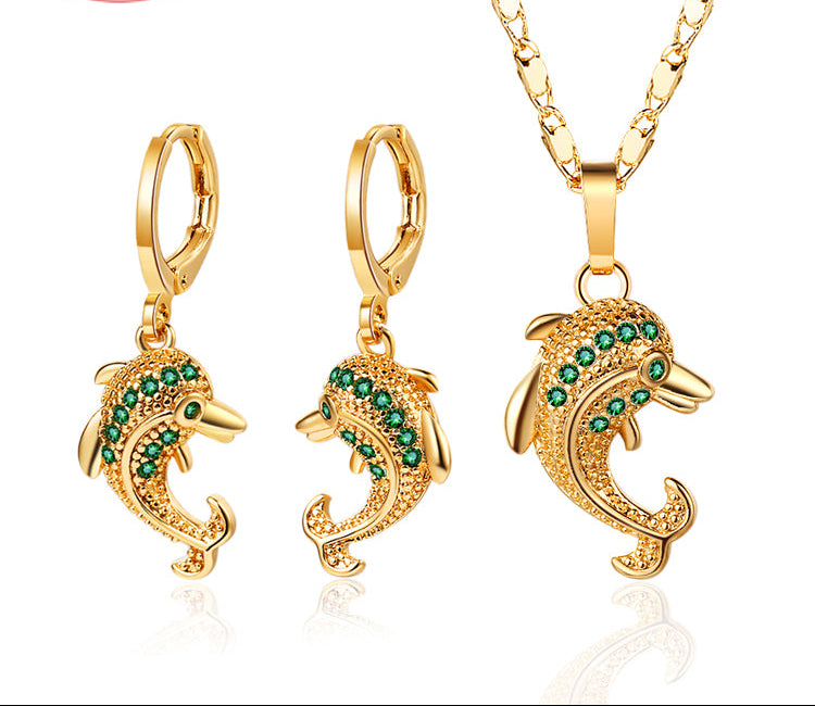 Gold dolphin earrings and necklace with green stones on a white background