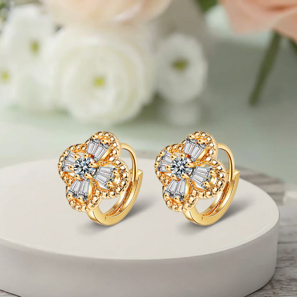 Gold earrings with gemstones on a white surface with a blurred floral background